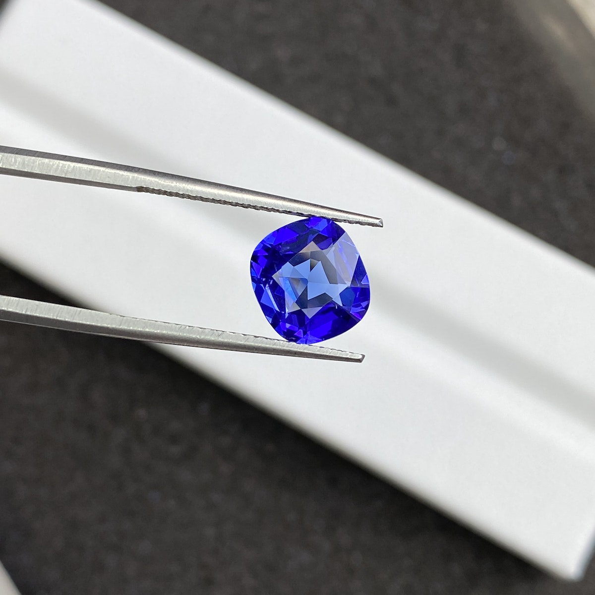 Une paire de pinces tient une pierre précieuse Tanzanite bleue vibrante de 2,44 ct de Bonnot Paris sur un fond noir et blanc flou.