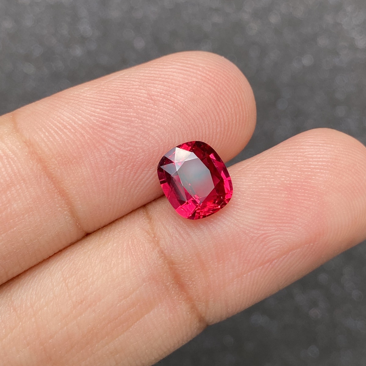 Une main tient une pierre précieuse Rubis du Mozambique · 2,57 ct de Bonnot Paris sur un fond gris texturé, mettant en valeur sa teinte rose foncé et ses facettes exquises.