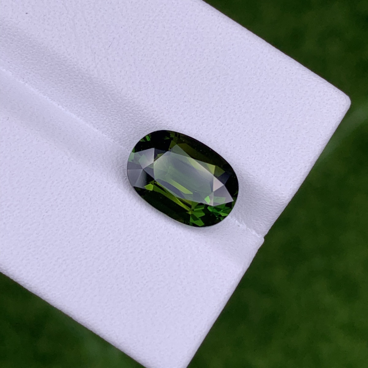 La Tourmaline Chrome · 3,04ct de Bonnot Paris est une pierre précieuse verte taille émeraude avec un bord sombre, présentée sur une surface blanche avec un fond vert flou.