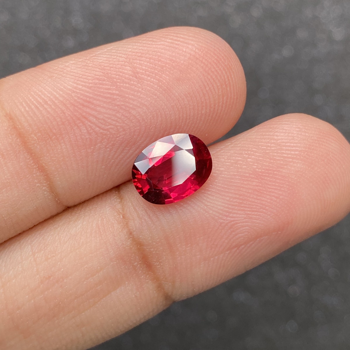 Les doigts tiennent un Rubis du Mozambique de 2,59 carats de Bonnot Paris, mettant en valeur sa pierre précieuse ovale facettée rouge foncé sur un fond sombre flou.