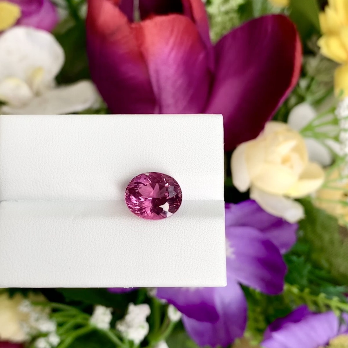 La Tourmaline Rubellite 4,35ct de Bonnot Paris est présentée sur un fond blanc, avec un arrangement floral vivant de fleurs violettes, rouges, blanches et jaunes rehaussant la scène.
