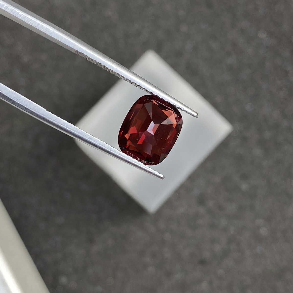 Une paire de pinces tient une pierre précieuse Spinelle Rouge rectangulaire facettée de 2,3 ct de couleur rouge foncé de Bonnot Paris au-dessus d'un arrière-plan flou.