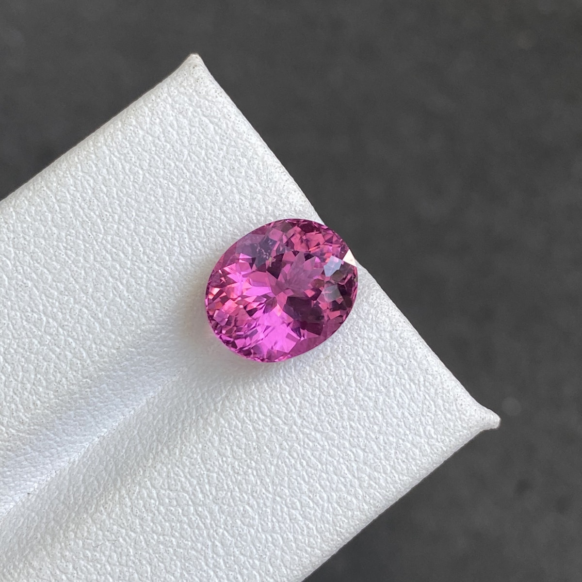 Un gros plan de la tourmaline rubellite Bonnot Paris · 4,35 ct sur une surface blanche texturée sur un fond sombre et flou capture sa teinte rose étincelante, sa couleur vibrante et ses facettes réfléchissant la lumière.