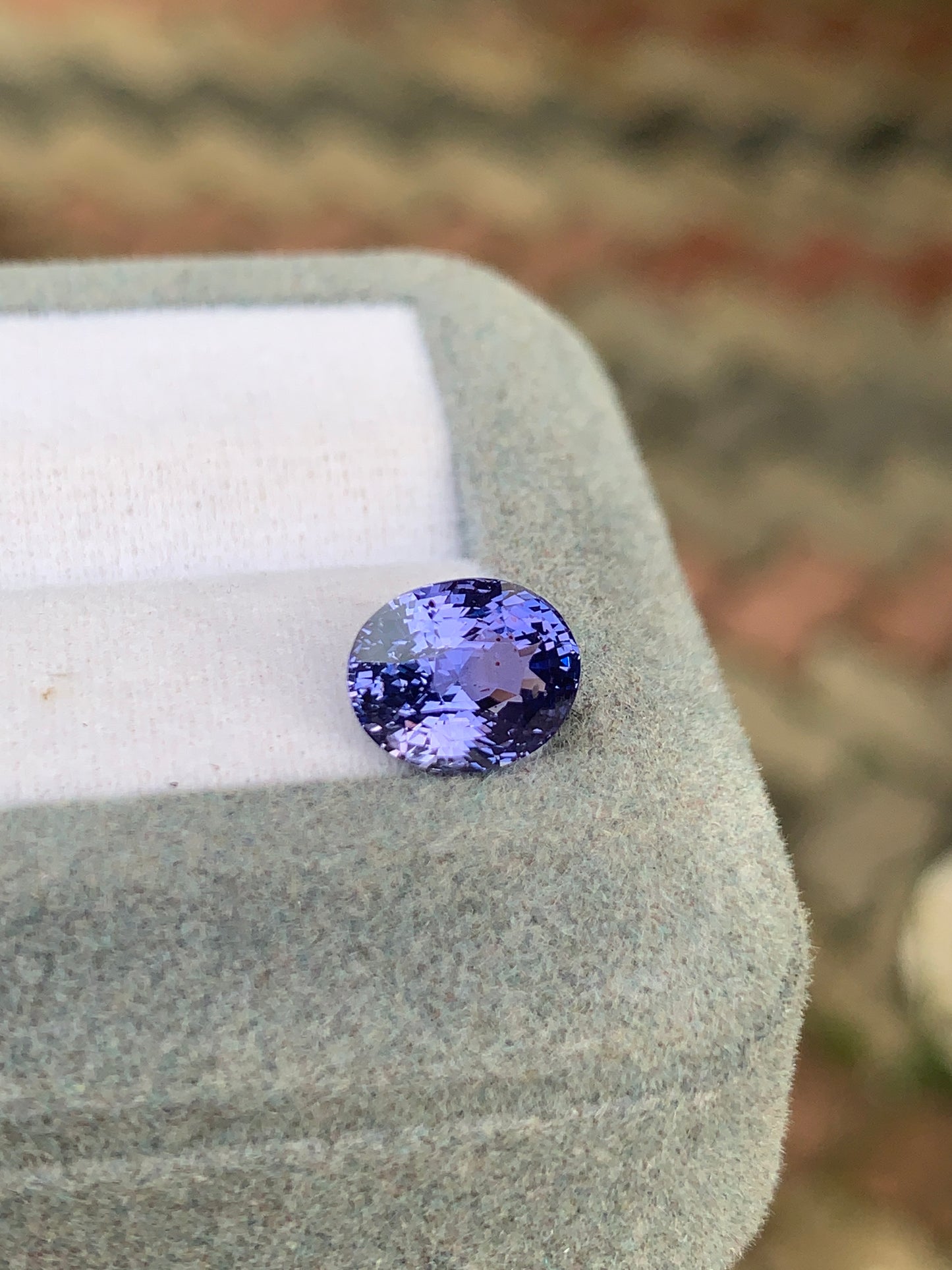 Gros plan d'un saphir violet rond de 3,52 carats, non chauffé, de Bonnot Paris, en provenance du Sri Lanka, présenté sur un doux coussin gris. La pierre scintillante présente des reflets internes complexes sur un fond flou.