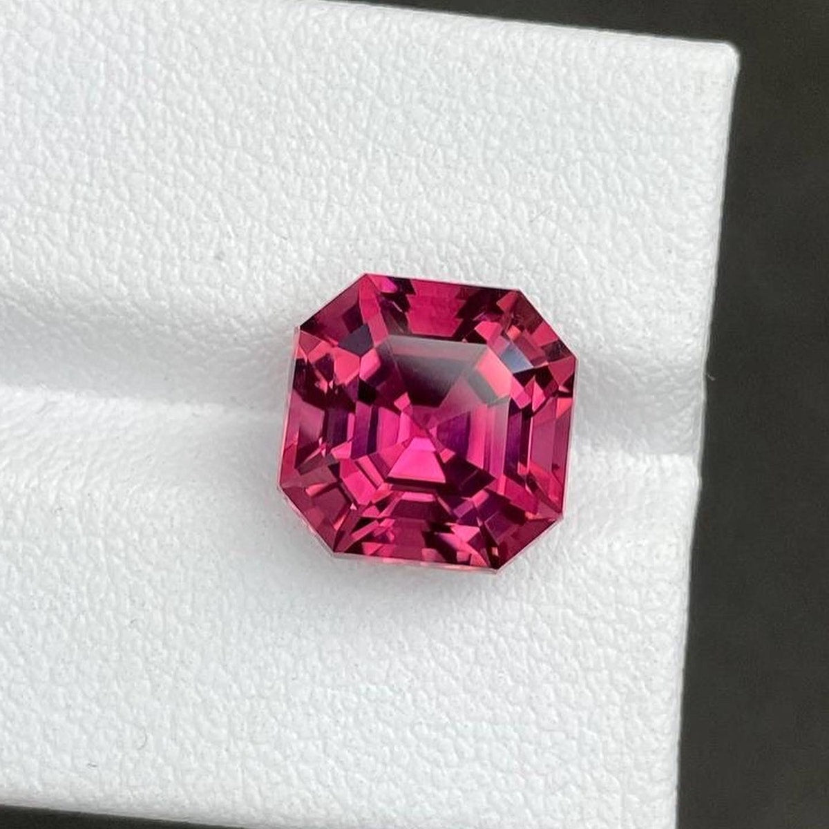 Une tourmaline rose d'un rose éclatant de 6,79 carats de Bonnot Paris est mise en valeur sur une surface blanche texturée. Ses facettes taille émeraude captent la lumière, sublimant sa clarté et sa teinte rose profond.