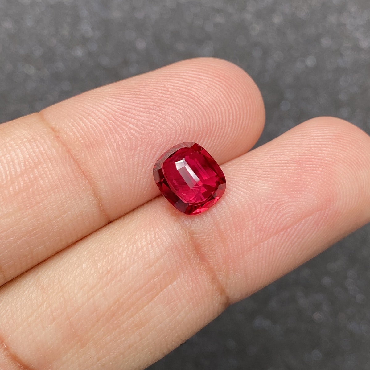 Une main tient un Rubis du Mozambique Bonnot Paris, 2,57 ct, dont le fond flou met en valeur sa couleur profonde et sa taille facettée.