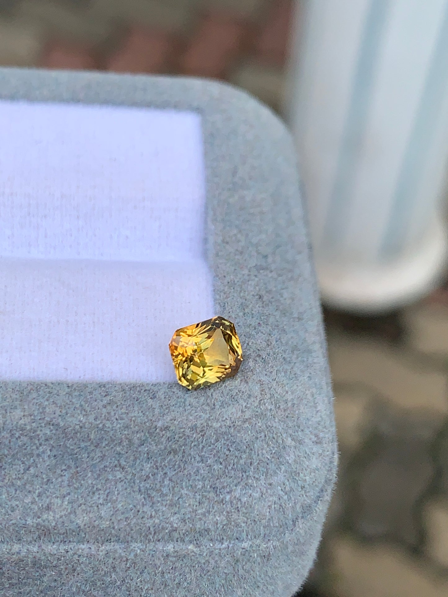 Un Saphir bicolore • 1,10ct de Bonnot Paris repose sur un écrin gris clair, son éclat jaune scintillant sur le fond flou, mettant en valeur son élégance intemporelle.