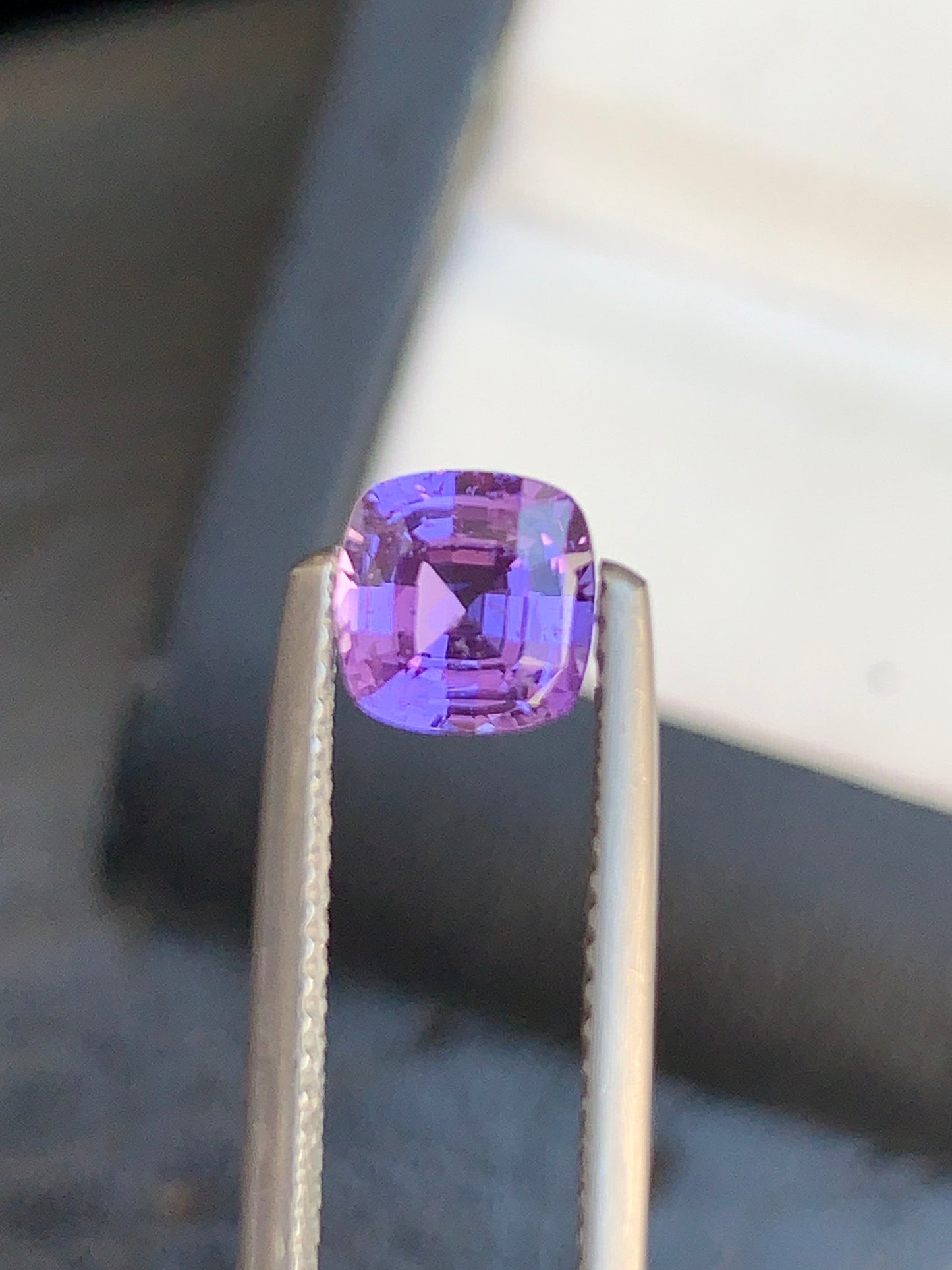 Gros plan sur la pierre précieuse Saphir Violet de Bonnot Paris de 1,5 carat, taille coussin et maintenue par une pince métallique. Cette magnifique pierre scintille de clarté sur un fond flou, évoquant le charme des trésors cachés de Madagascar.