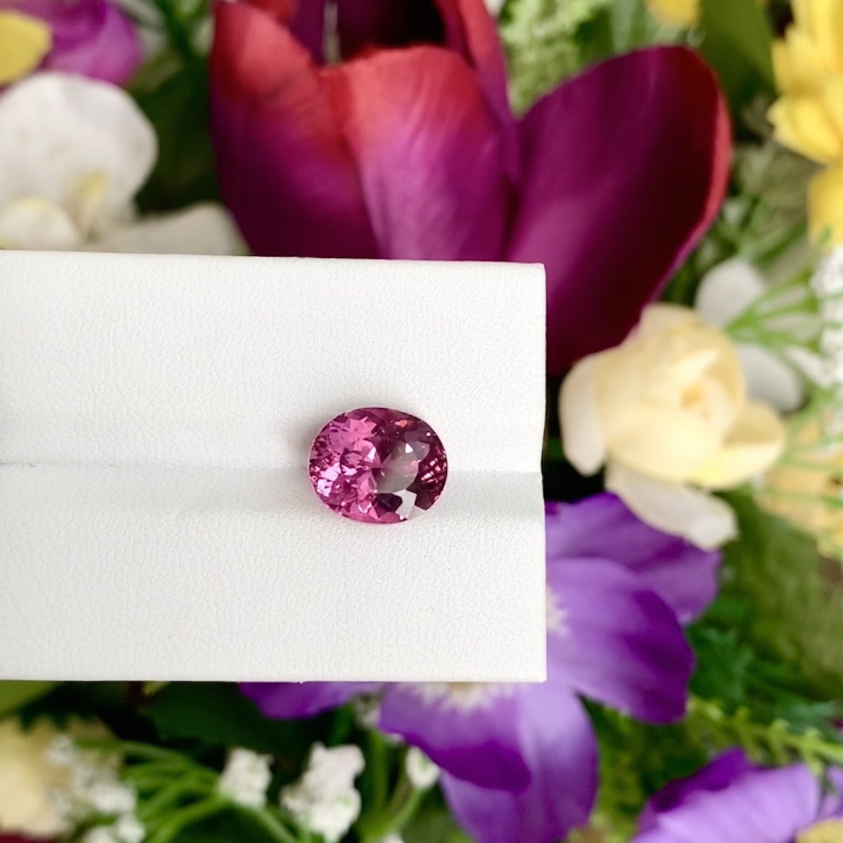 La Tourmaline Rubellite de Bonnot Paris, pèse 4,35 ct et est élégamment présentée sur une surface blanche avec des fleurs rouges et violettes en arrière-plan.
