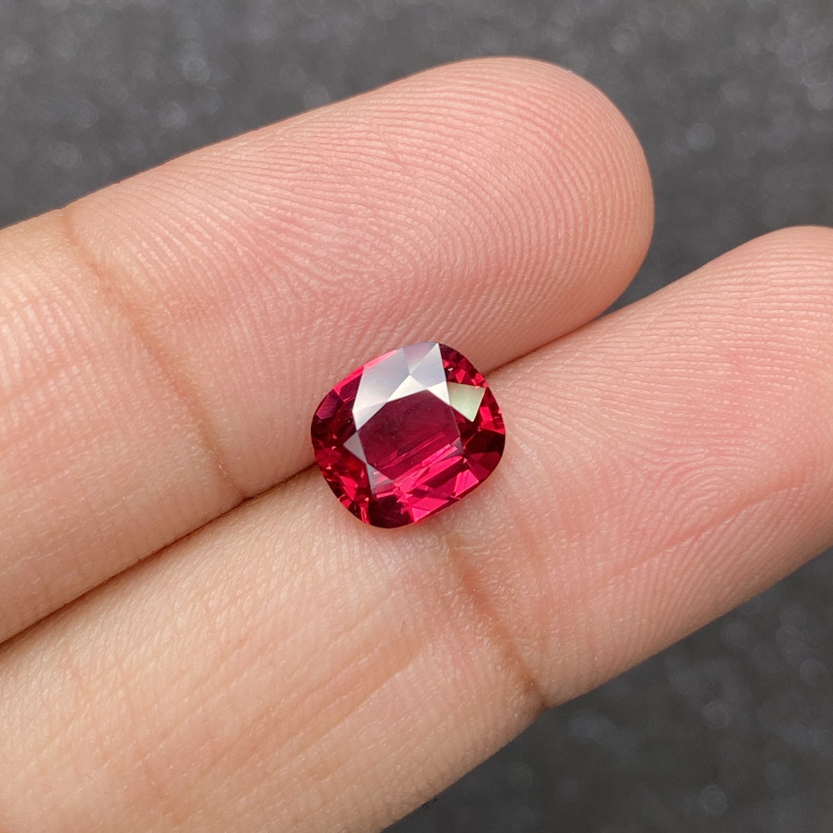 Un gros plan montre une main tenant la pierre précieuse Rubis du Mozambique de 2,57 ct de Bonnot Paris sur un fond sombre, sa surface rouge rosé facettée scintillant de couleurs et de clarté vibrantes.