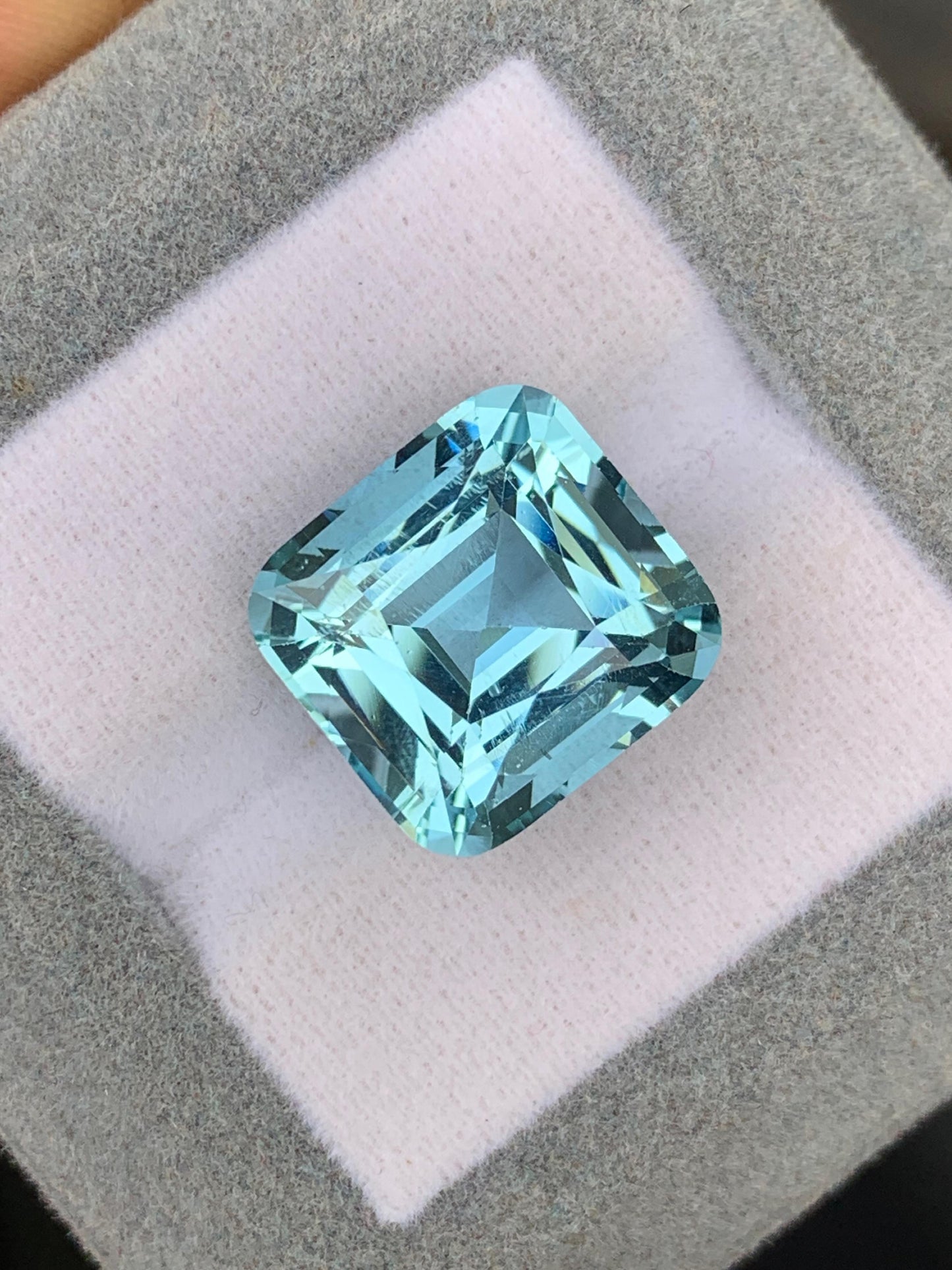 Un gros plan sur l'Aigue-Marine • 12,58ct deBonnot Paris révèle ce bijou unique aux facettes reflétant la lumière dans des nuances de bleu envoûtantes, sur fond gris et blanc coussiné.