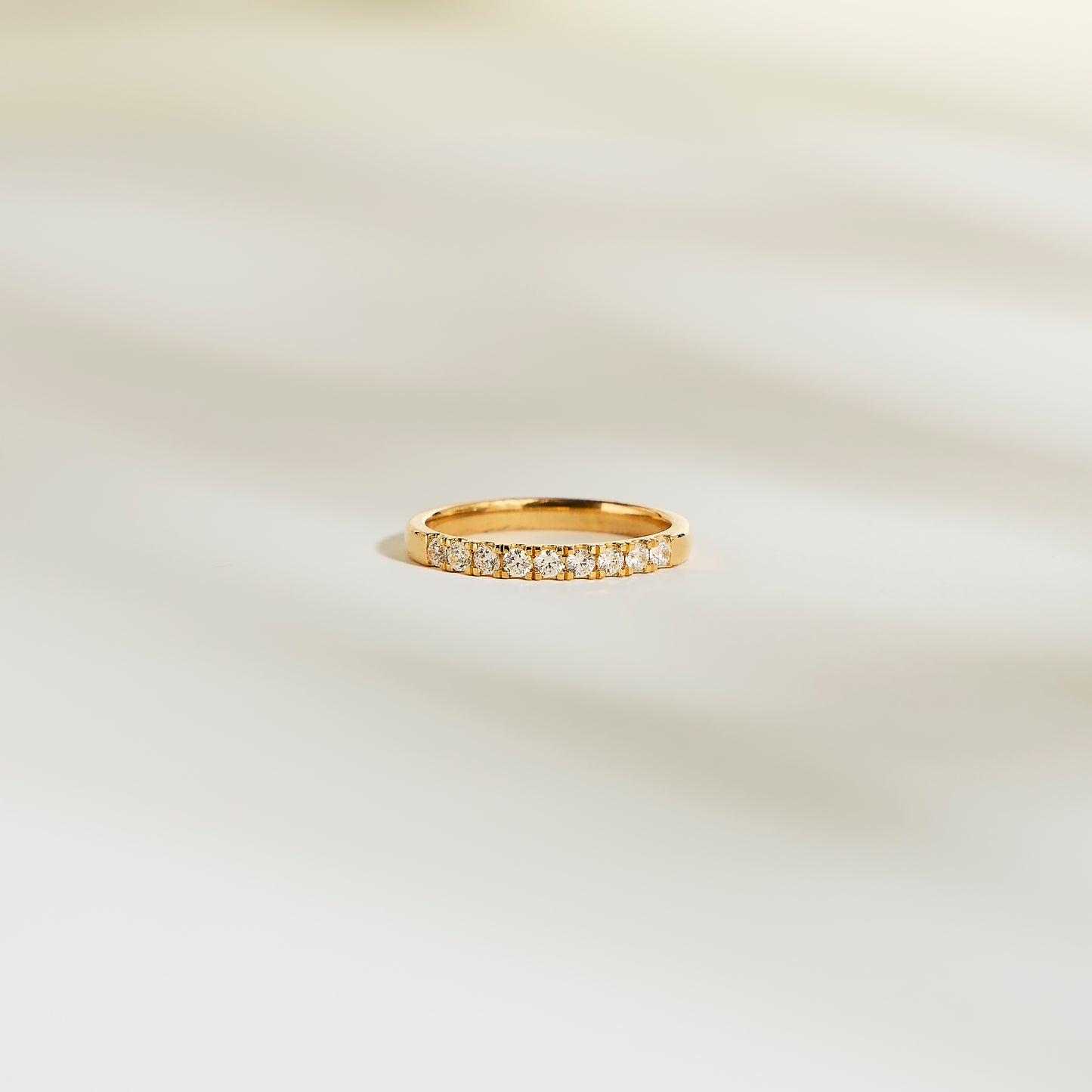 L'Alliance La Discrète de Bonnot Paris arbore une bague en or sertie de petits diamants naturels scintillants. Son design taille rond-brillant, d'une élégante simplicité, capte magnifiquement la lumière sur un fond clair et légèrement flou.