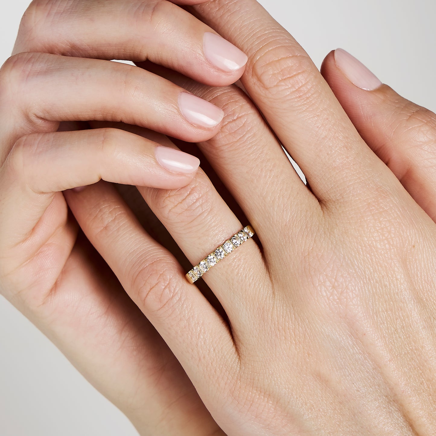 Gros plan d'une main aux ongles impeccablement manucurés, portant l'Alliance La Majestueuse de Bonnot Paris. La bague, ornée de petites pierres taille brillant d'une pureté de couleur G/H SI, scintille à l'annulaire gauche sur un fond clair.