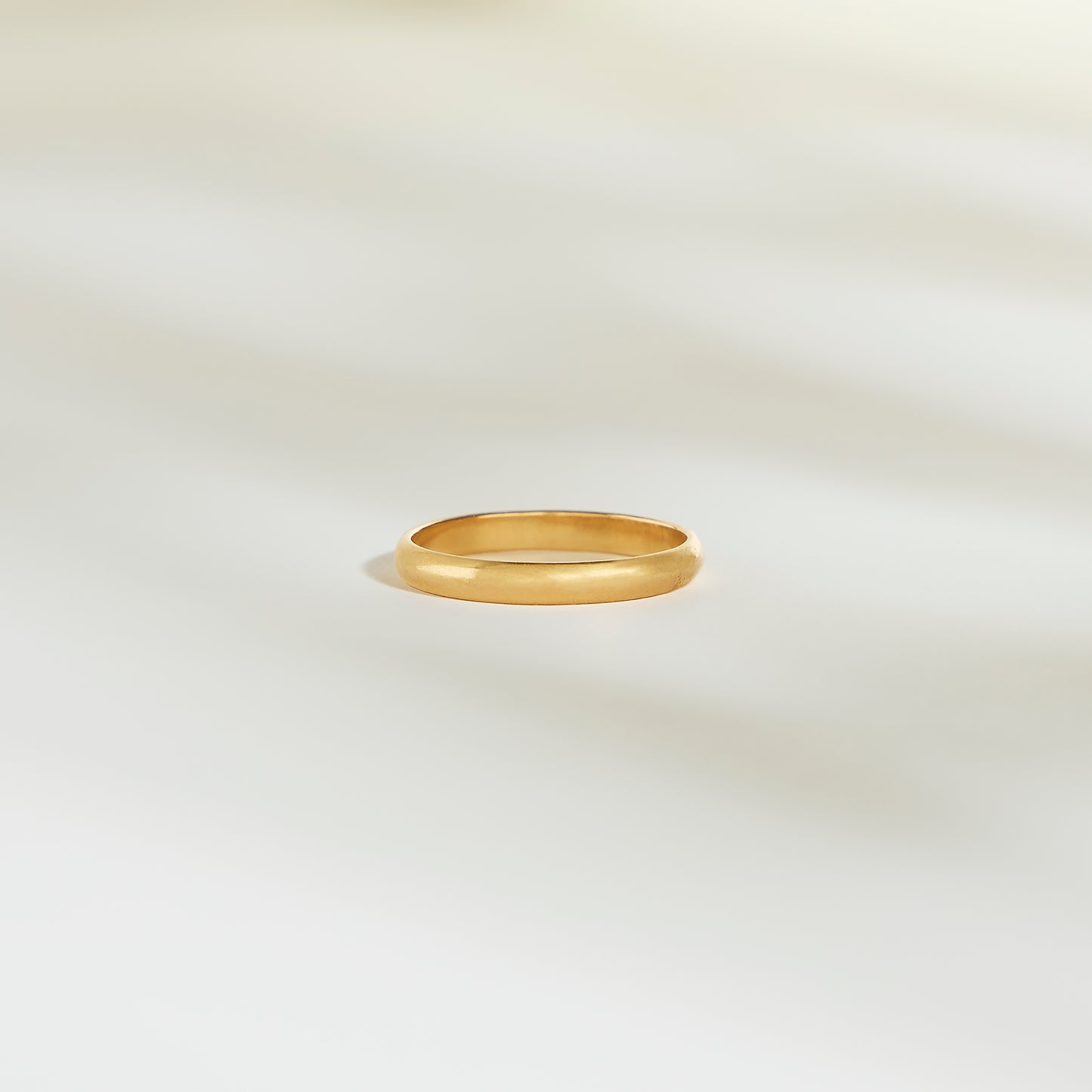 L'Alliance L'Authentique, un simple anneau en or signé Bonnot Paris, repose sur une surface pâle et légèrement éclairée. Les ombres subtiles qui l'entourent créent une atmosphère calme et élégante.