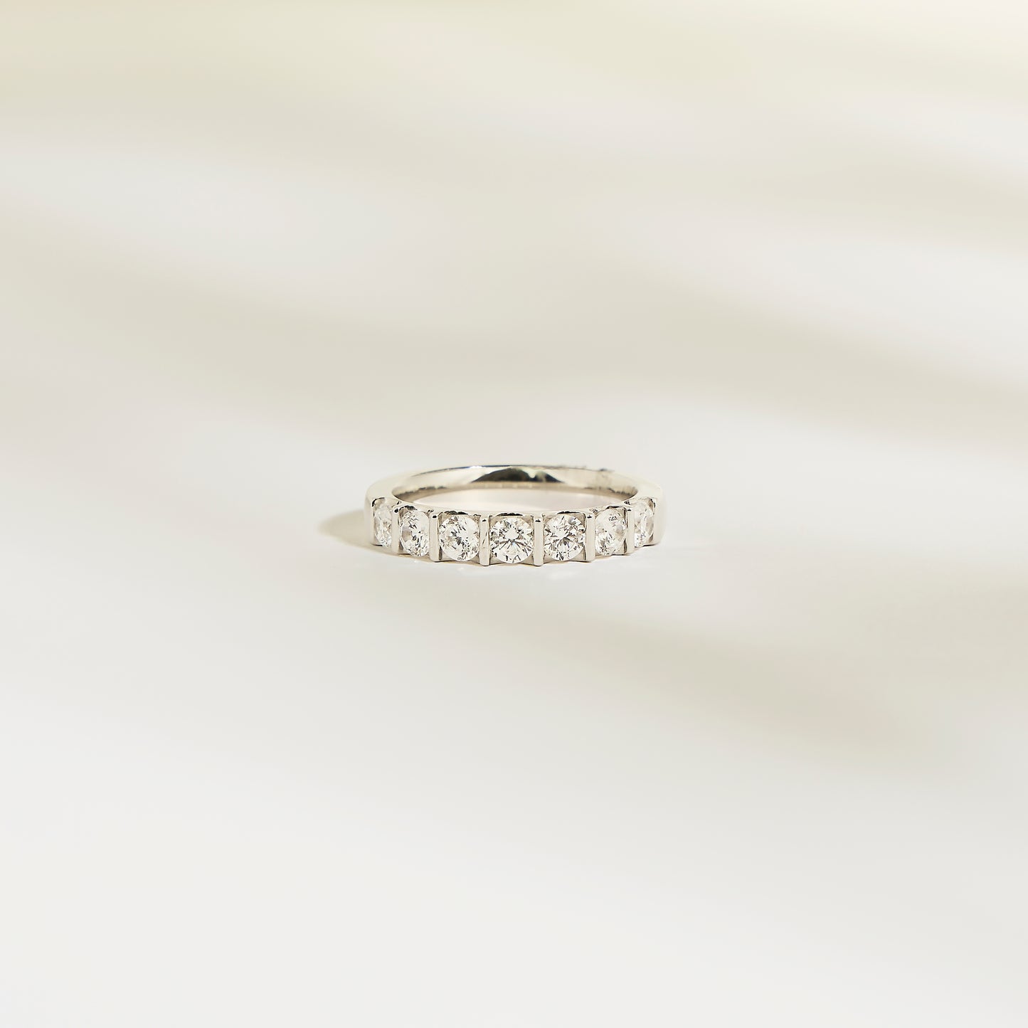 L'Alliance La Subtile de Bonnot Paris est une bague en argent sertie de pierres taille carrée, semblables à des diamants. Son éclat brillant évoque un luxe discret, issu d'une collection exquise. Elle repose sur une surface lisse et légère, avec des ombres douces et floues en arrière-plan.