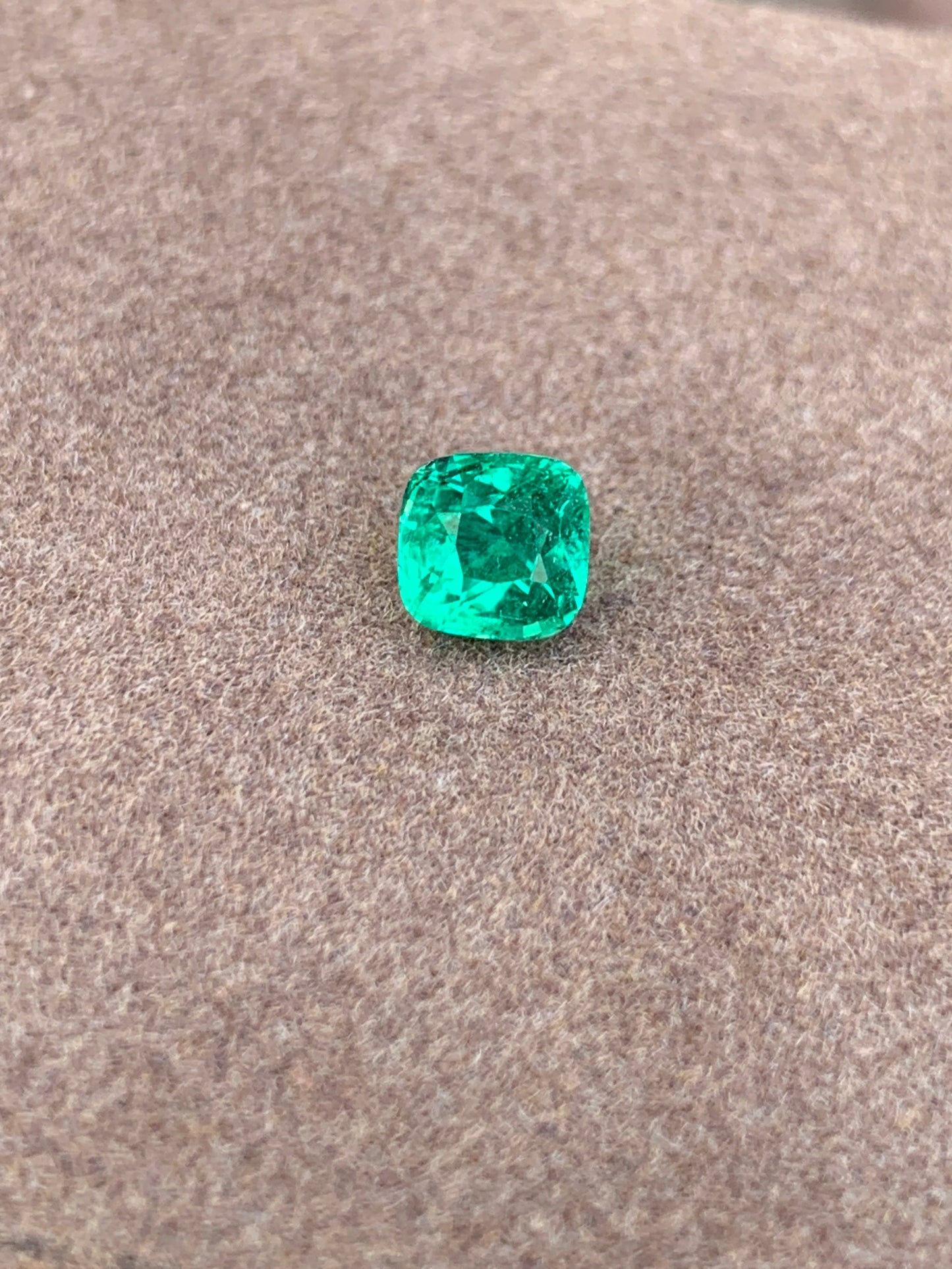 L'Émeraude taille coussin • 1,15ct de Bonnot Paris met en valeur sa teinte verte lumineuse sur une surface brune douce et texturée, reflétant magnifiquement la lumière de ses facettes.