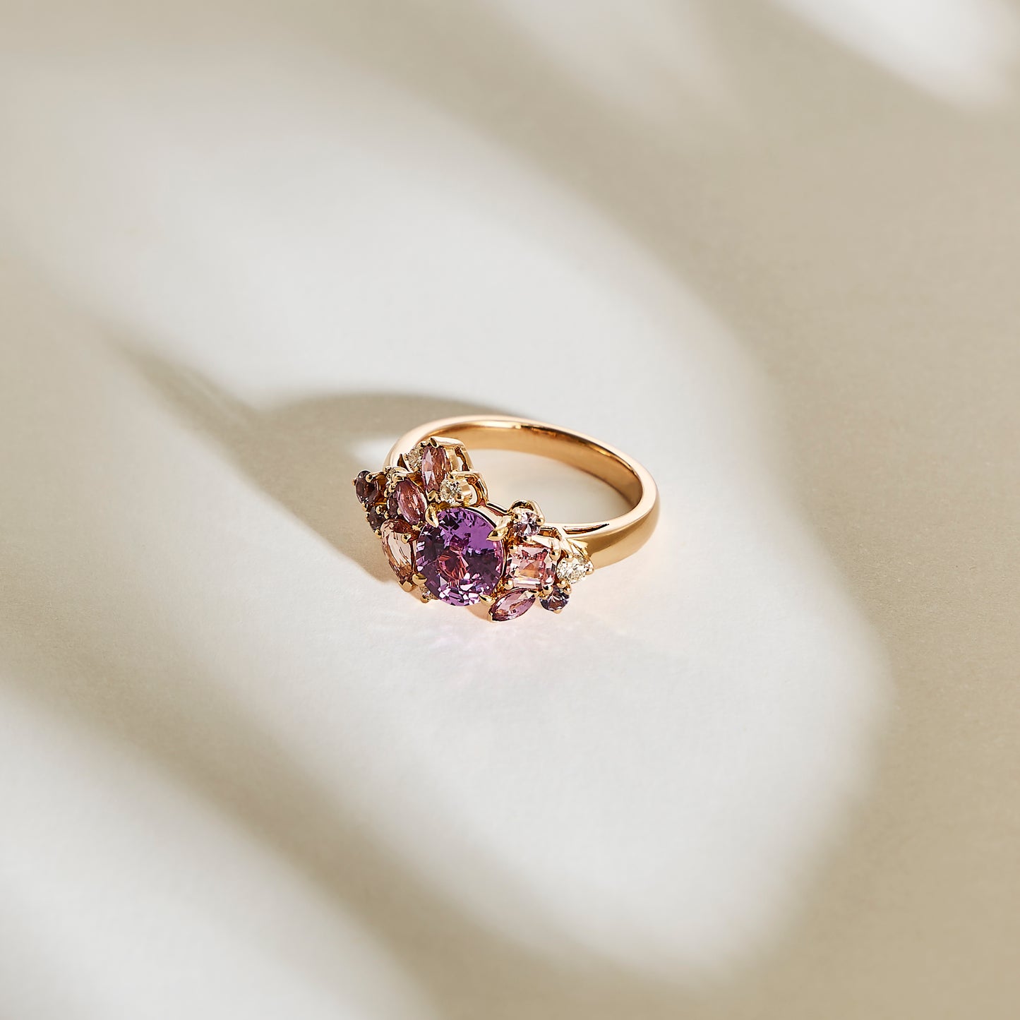 Le Purple Bloom - Saphir de Bonnot Paris est présenté sur une surface blanche doucement éclairée, son anneau en or orné de pierres précieuses violettes et de diamants délicats, projetant des ombres douces pour un motif subtil.