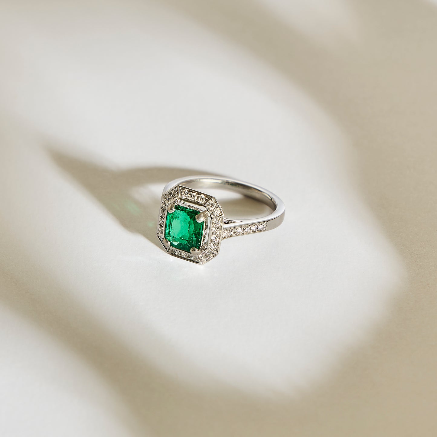 La Bague Émeraude • 1,22 carat de Bonnot Paris est une bague en argent de style Art Déco, ornée d'une émeraude verte rectangulaire de Zambie, flanquée de petits diamants. Sur un fond clair, de subtiles ombres soulignent son design complexe.