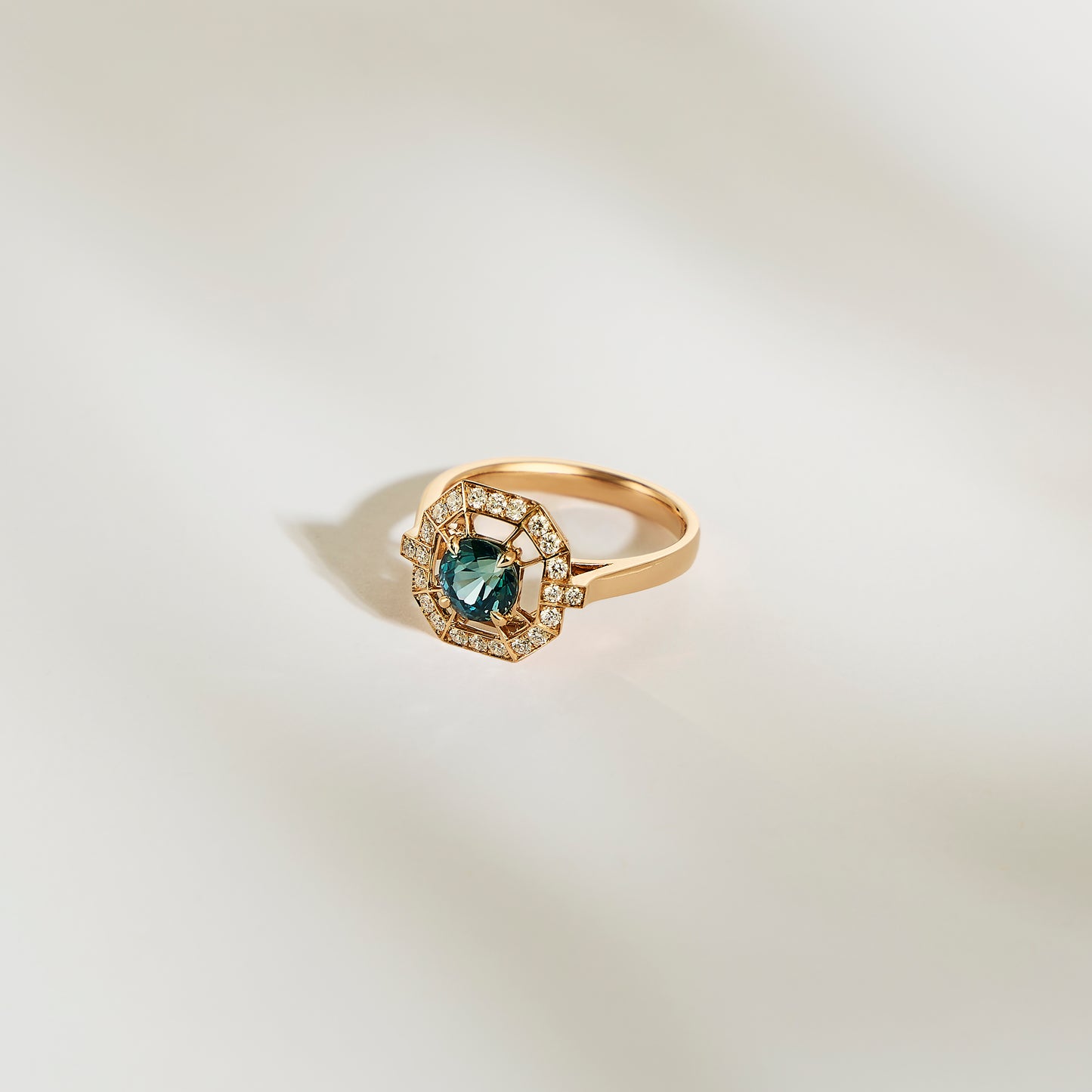 La Bague Saphir Teal • 1,16ct de Bonnot Paris présente un large saphir bleu sarcelle entouré de diamants blancs étincelants, élégamment présenté sur un fond doux et clair.
