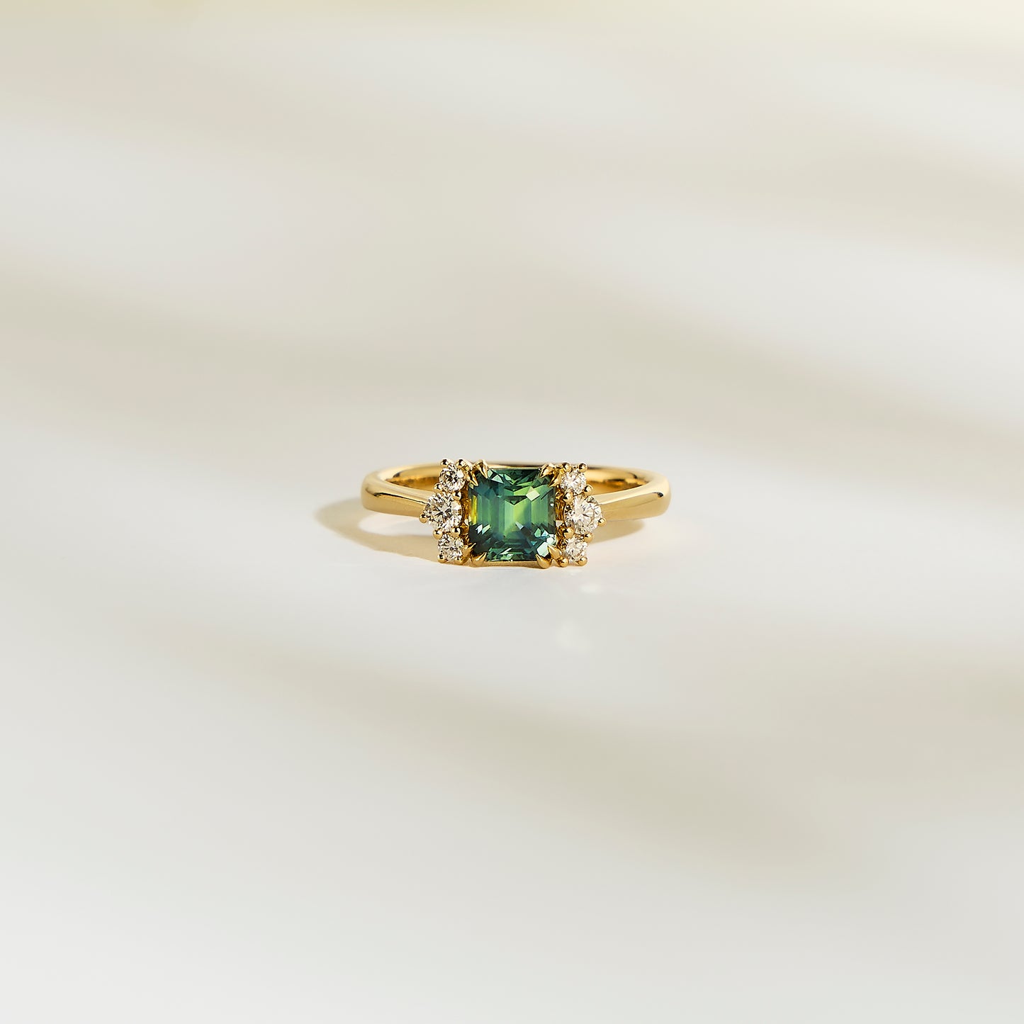La Bague Bonnot Paris Saphir Teal • 1,24 ct présente une pierre précieuse sarcelle carrée flanquée de petits diamants blancs étincelants sur une bande lisse et de couleur claire.