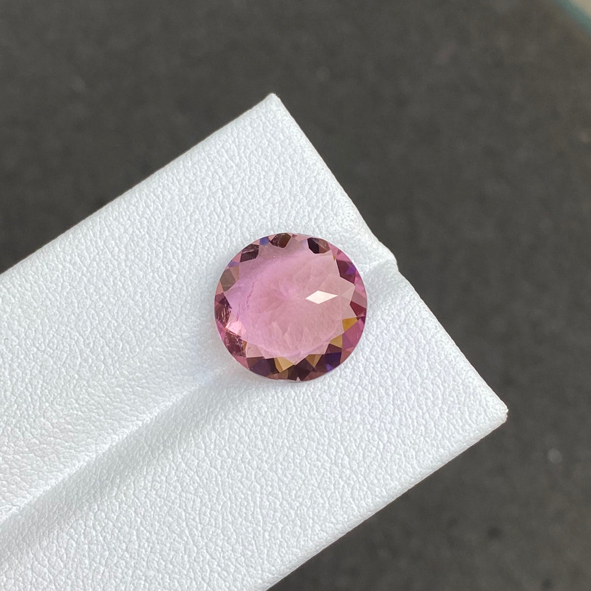 La Tourmaline Cuprifère, une pierre rose ronde facettée de 5,22 carats signée Bonnot Paris, est présentée sur un support blanc sur fond sombre. Sa surface reflète magnifiquement la lumière, soulignant sa clarté et sa taille exquise.