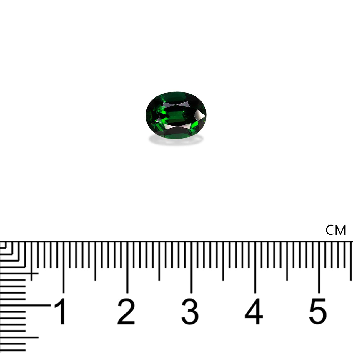 Une petite tourmaline chrome ovale de Bonnot Paris est posée sur un fond blanc. Une règle graduée en centimètres permet de visualiser la couleur vert foncé et intense de cette pierre de 1,2 cm de long et sa surface facettée.