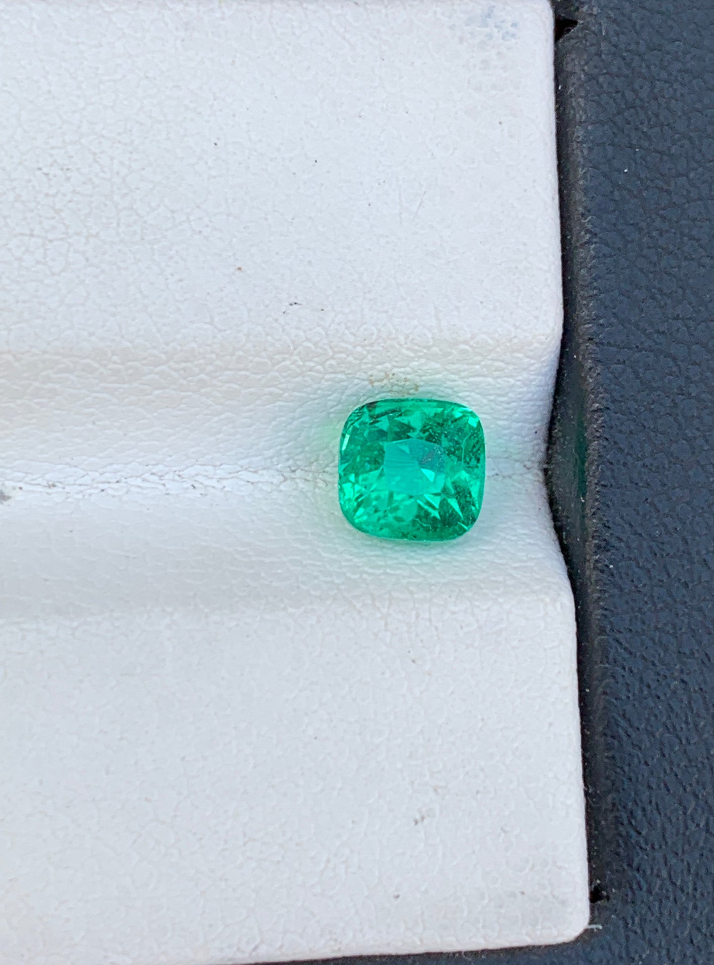 La pierre précieuse Émeraude Bonnot Paris • 1,15 ct avec une taille coussin repose sur une surface coussinée blanche sur un fond gris foncé.
