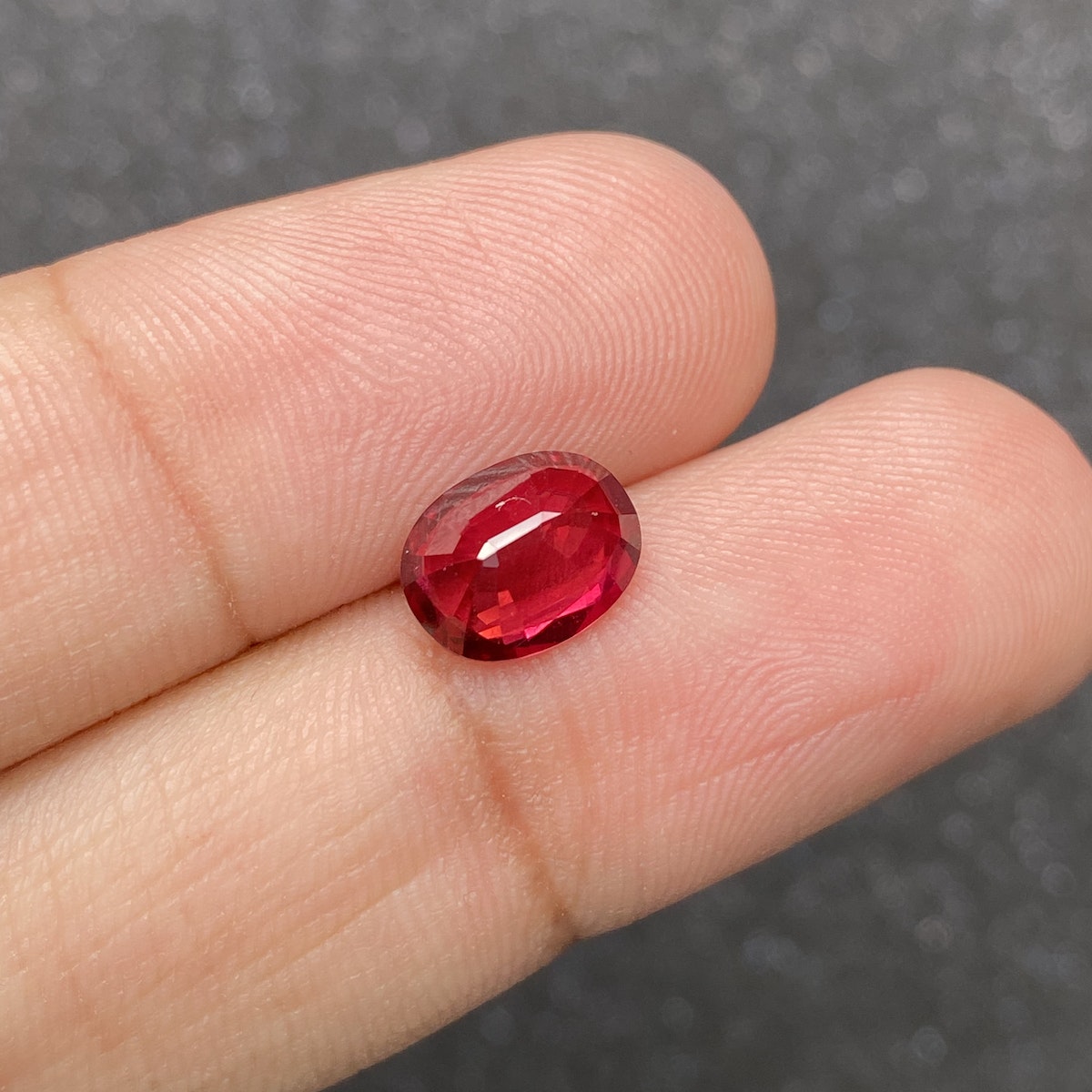 Le Rubis du Mozambique, une pierre ovale de 2,59 carats de Bonnot Paris, se détache sur un fond gris flou.