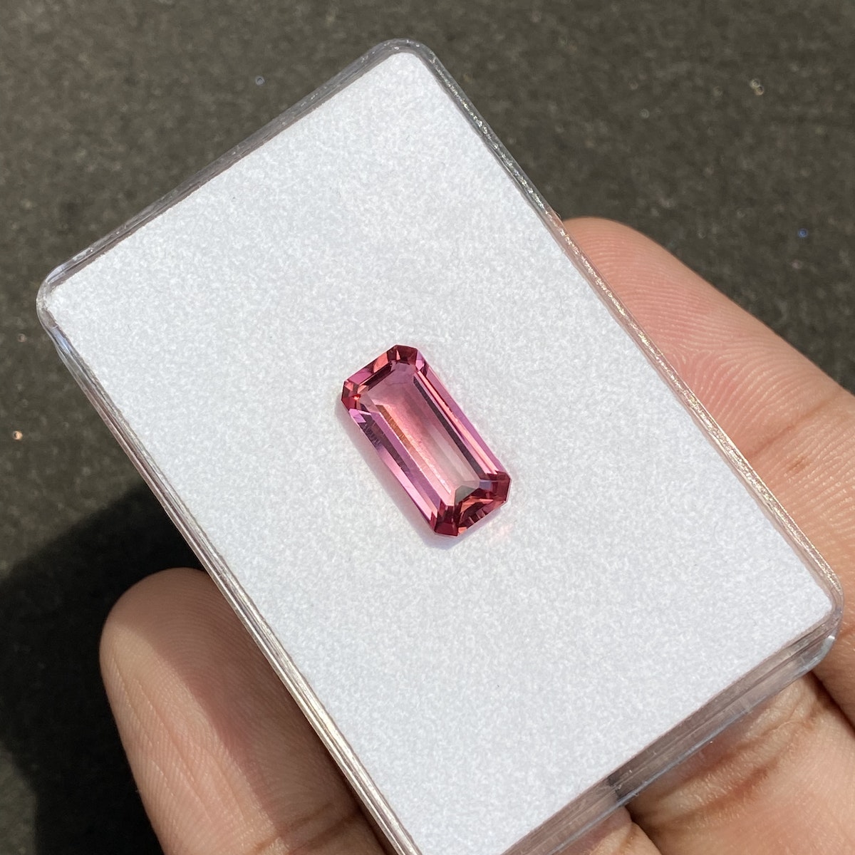 Une aiguille présente la Tourmaline Rose de Bonnot Paris, un boîtier transparent renfermant une pierre rose facettée de 3,95 carats sur fond blanc. La surface de la pierre scintille de lumière, accentuant ses arêtes sur le fond sombre.