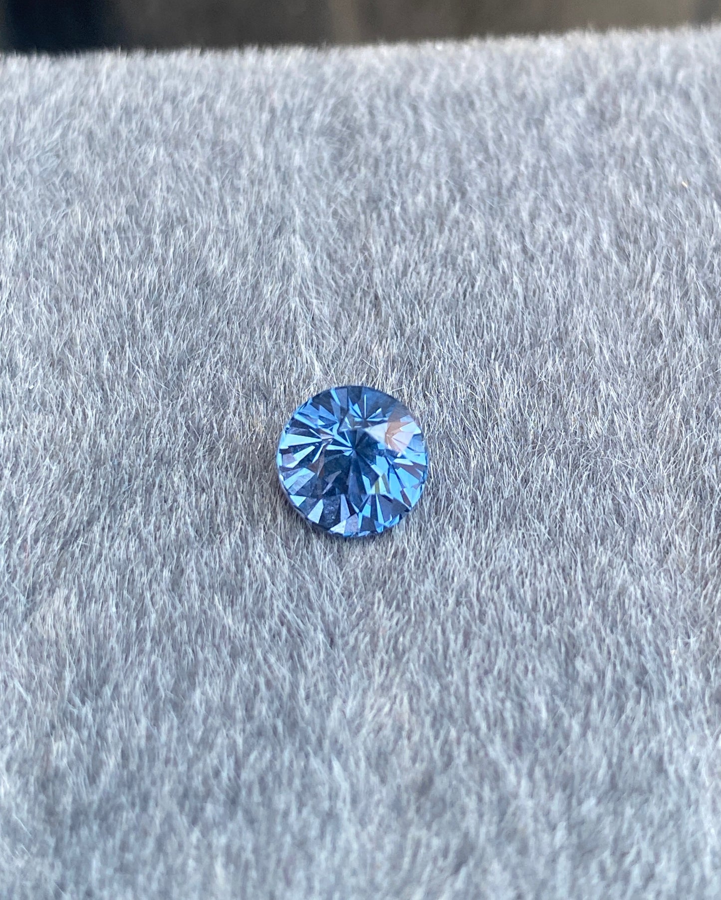 Le Spinelle Gris • 1,67 ct de Bonnot Paris, avec son design rond et taille brillant, repose sur une surface grise douce, affichant son éclat naturel à travers des facettes scintillantes.