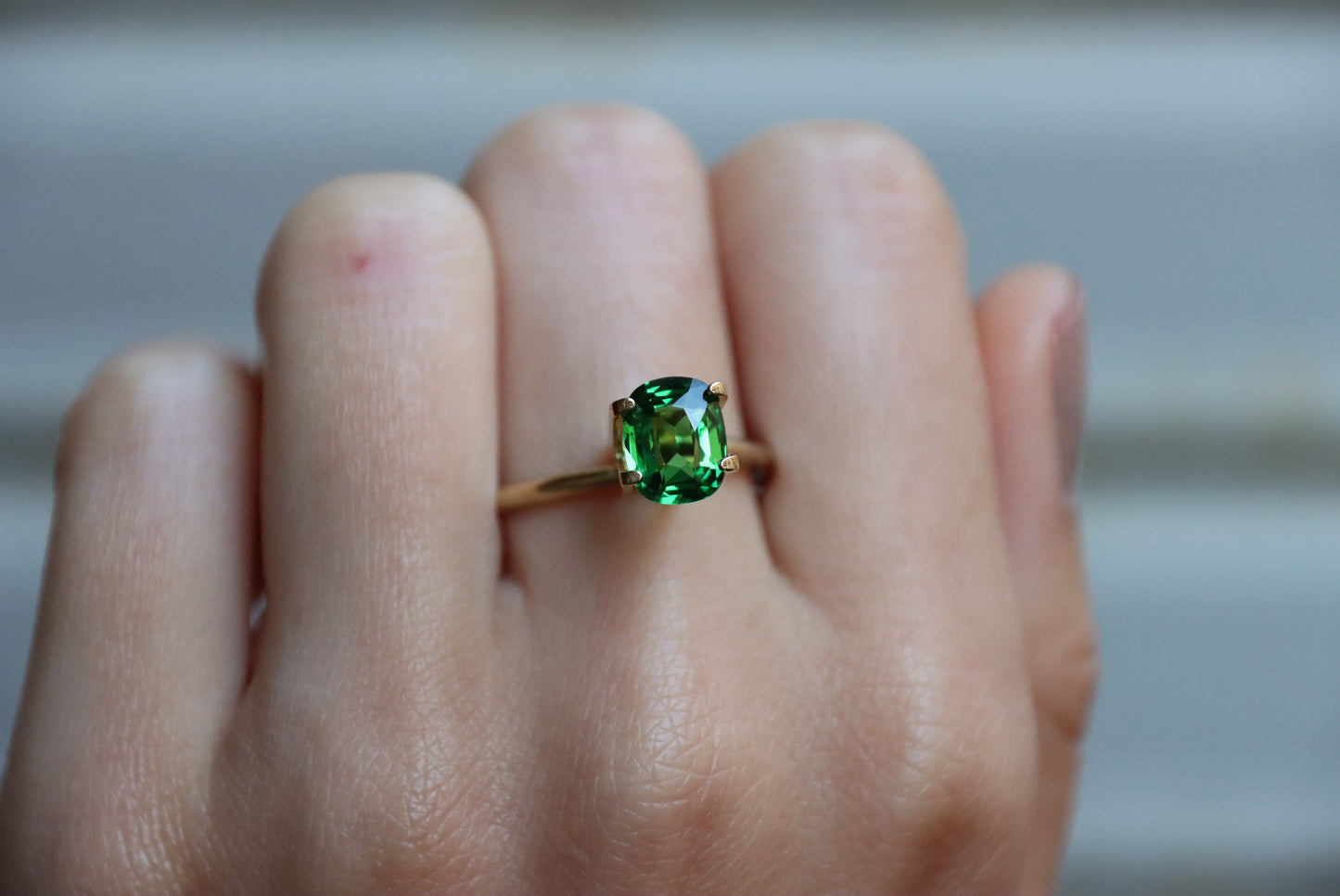 Une main présente une bague en or Bonnot Paris ornée d'une pierre précieuse Grenat Tsavorite verte ovale de 1,7 ct sur un fond neutre flou.