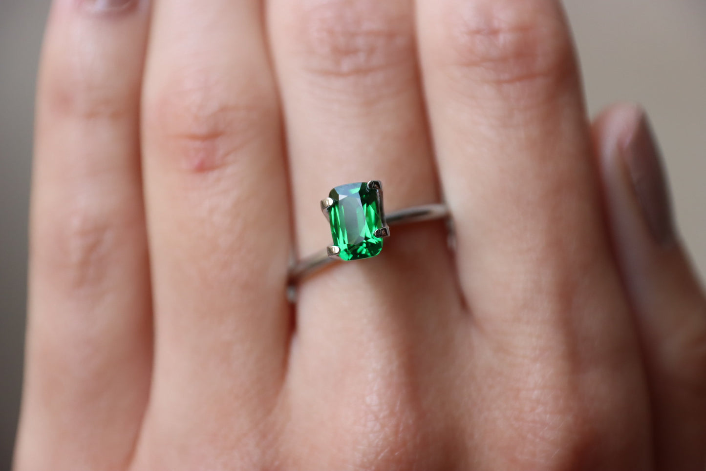 Une main met en valeur la Grenat Tsavorite de Bonnot Paris, une bague en argent avec une pierre précieuse verte taille émeraude (1,53 ct), sur un fond légèrement flou.