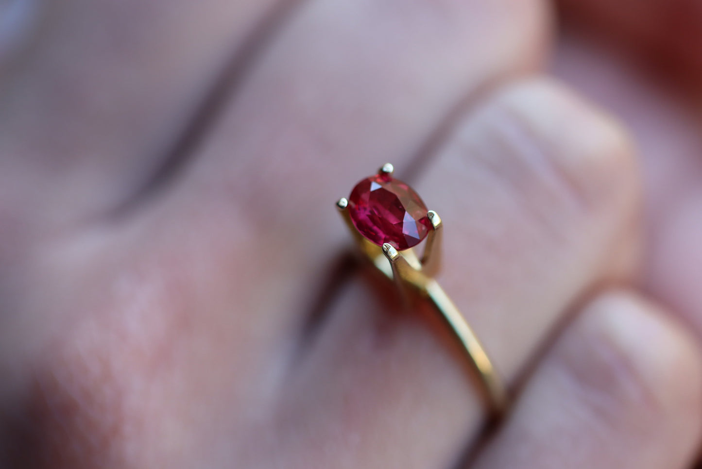 Gros plan d'une bague en or Bonnot Paris "Rubis du Mozambique · 1,52 ct" avec une pierre précieuse rouge ovale, sertie sur quatre griffes, portée sur un doigt à la peau délicatement focalisée, accentuant le design élégant et simple de la bague.