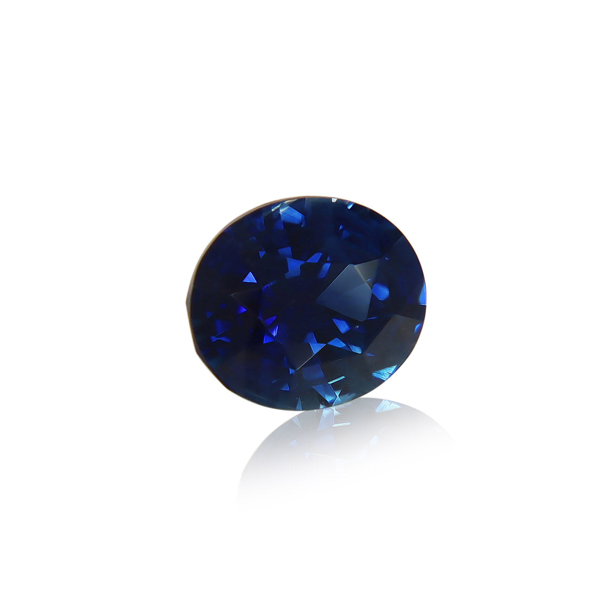 Le Saphir Bleu · 2,07ct de Bonnot Paris est une pierre précieuse facettée d'un bleu profond aux surfaces réfléchissantes, posée sur un fond blanc et projetant un reflet subtil en dessous.