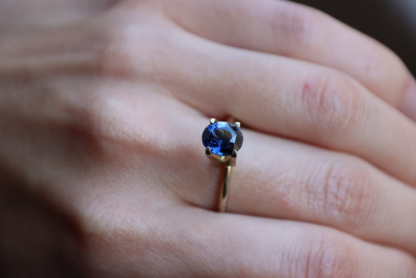 Gros plan d'une main ornée de la bague en or Saphir Bleu · 2,07 carats de Bonnot Paris sur le majeur, mettant en valeur la teinte bleu profond et la clarté de la pierre précieuse.