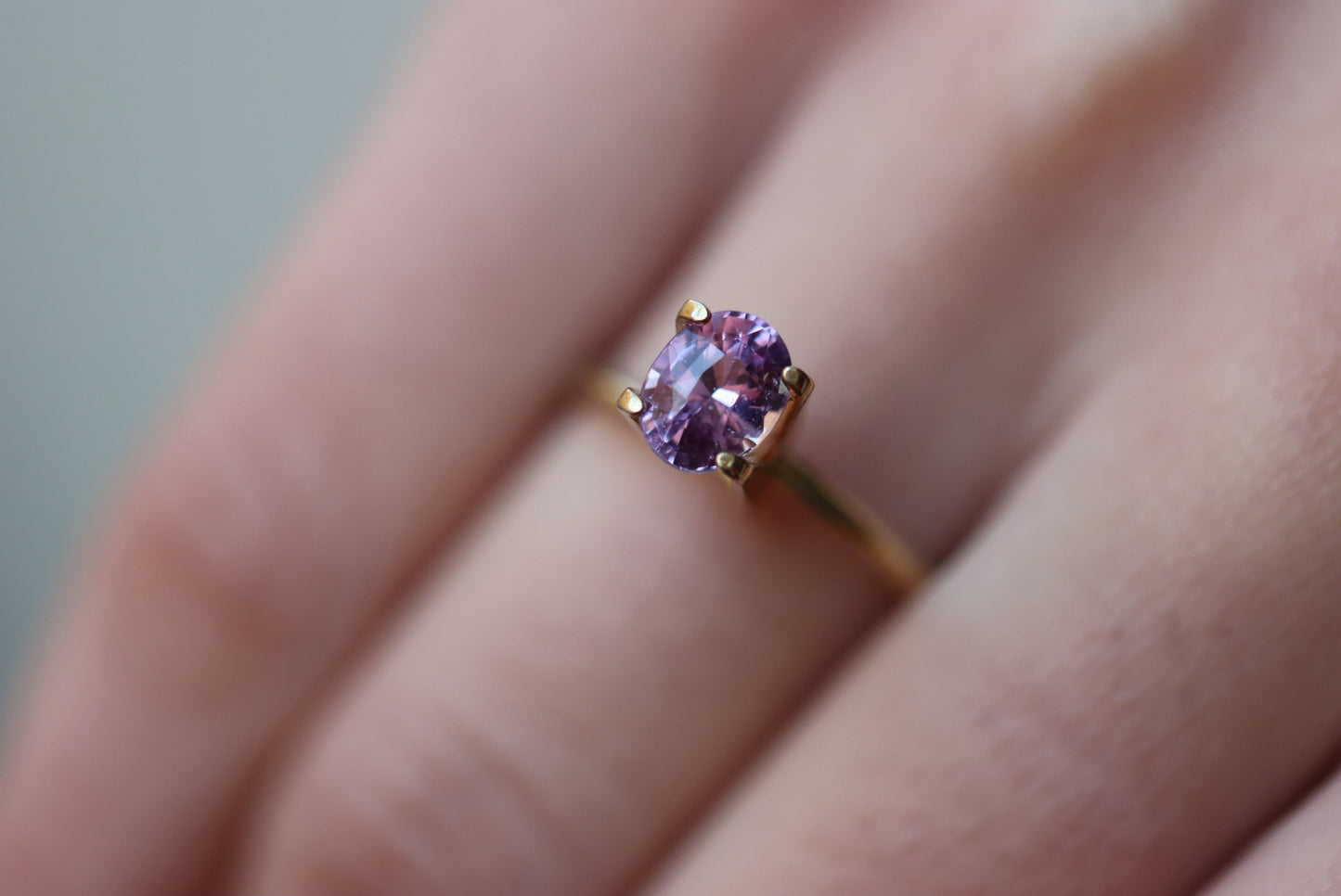 Une personne porte la bague Bonnot Paris Saphir Violet en or 1,59 carat, ornée d'une pierre violette ovale fixée par quatre griffes. Le fond légèrement flou met en valeur le design complexe et la couleur vibrante de la bague.