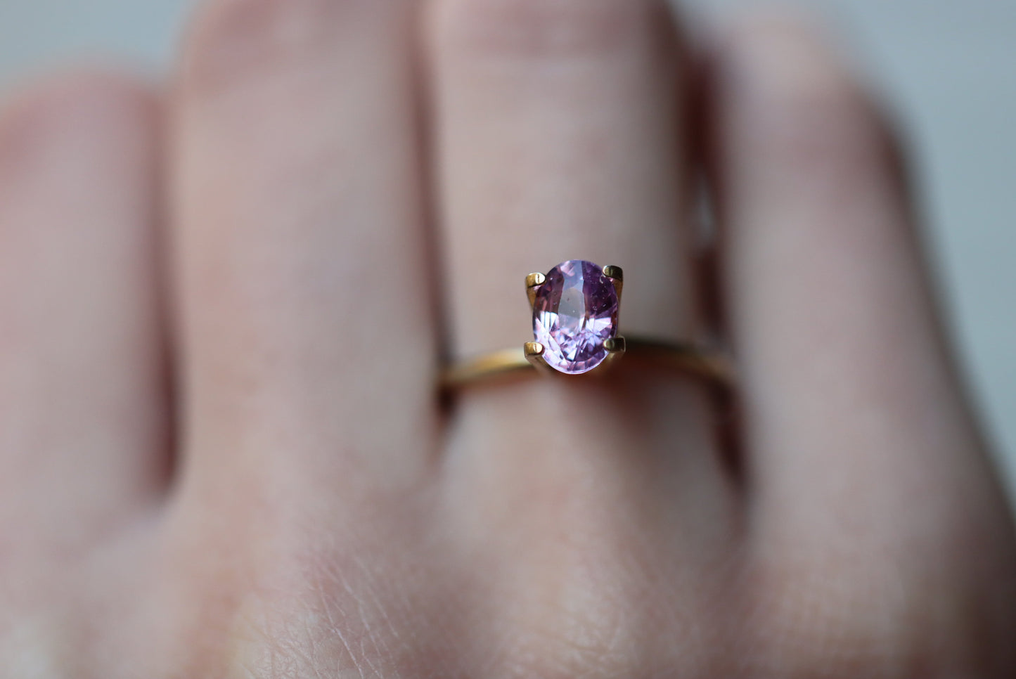 Un gros plan montre une main portant la bague Saphir Violet de Bonnot Paris, ornée d'une pierre précieuse rose taille ovale de 1,59 ct, sur l'annulaire avec un arrière-plan flou.