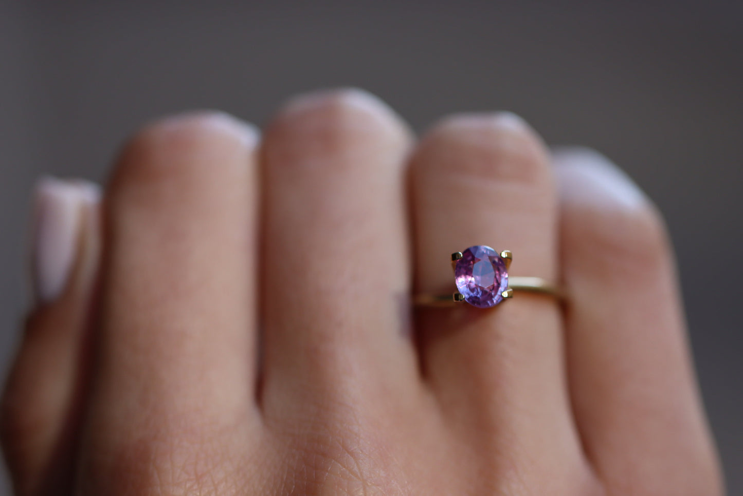 Une main met en valeur la bague en or Bonnot Paris « Saphir Violet · 1,51 ct » avec une pierre précieuse violette, sertie sur un fond légèrement flou qui met en valeur son design.