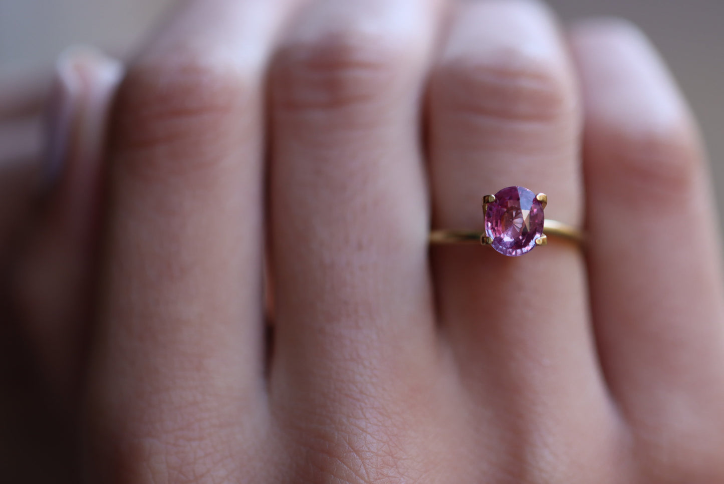 Gros plan sur une main ornée de la bague Saphir Violet 1,58 carat de Bonnot Paris, ornée d'une pierre rose ovale. La bague orne l'annulaire sur un fond légèrement flou, soulignant son élégance.