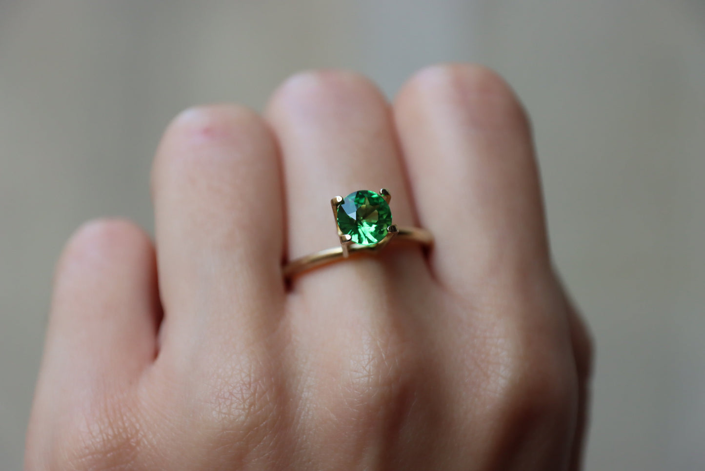 Une main présente une bague en or Bonnot Paris ornée d'une grosse pierre précieuse ronde Grenat Tsavorite de 1,49 ct sur l'annulaire, sur fond flou.