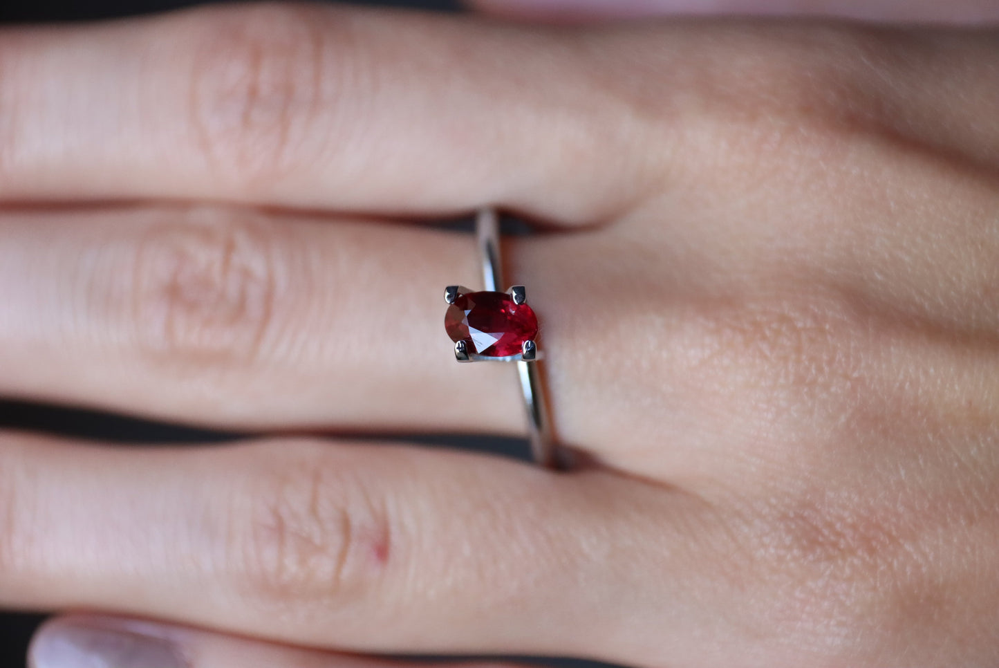 Une main portant la bague en argent Rubis du Mozambique de 1,01 ct de Bonnot Paris avec une pierre précieuse rouge de forme ovale dans un sertissage à quatre griffes, sur un fond légèrement flou.