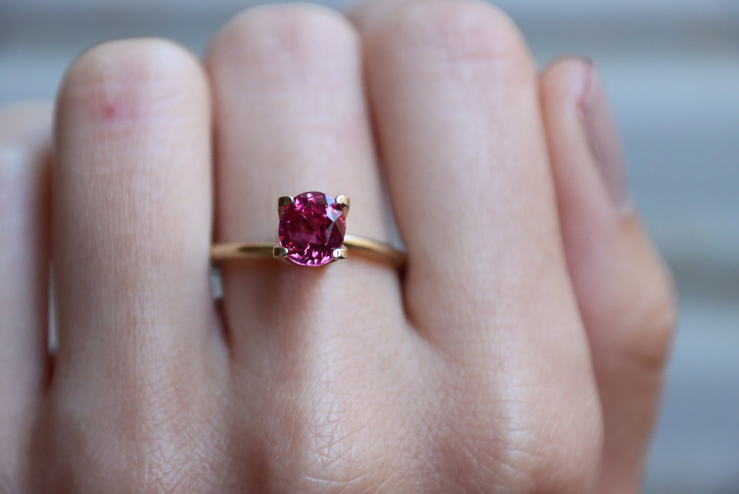 Une main portant la bague en or Bonnot Paris « Rubis de Birmanie · 1,68 ct » avec une pierre précieuse rose ovale est représentée sur l'annulaire sur un fond gris légèrement flou.