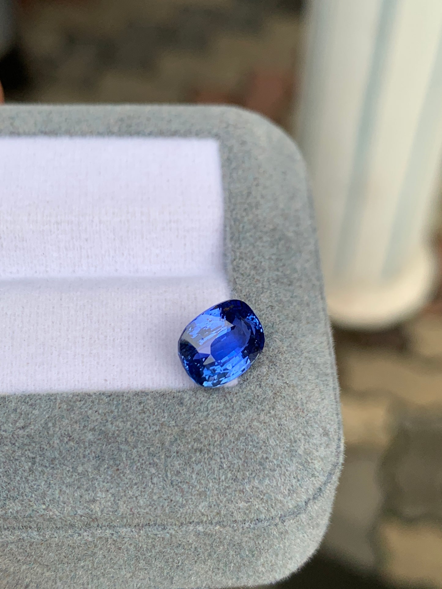 Le Saphir Bleu · 3,05 carats de Bonnot Paris scintille sur un écrin gris clair à l'intérieur blanc. Ses facettes taille coussin rehaussent sa couleur vive, reflétant le charme du Sri Lanka, sur un fond subtilement flou.