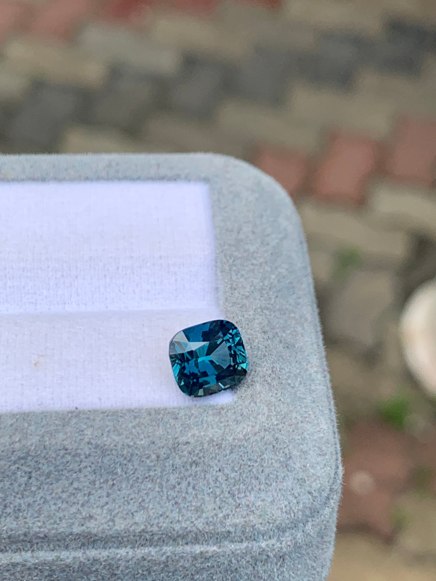 La pierre précieuse Saphir Teal de 2,50 carats de Bonnot Paris, provenant de Madagascar, est sertie sur une vitrine grise au fond à motifs flous, hypnotisant tout le monde par sa teinte enchanteresse.