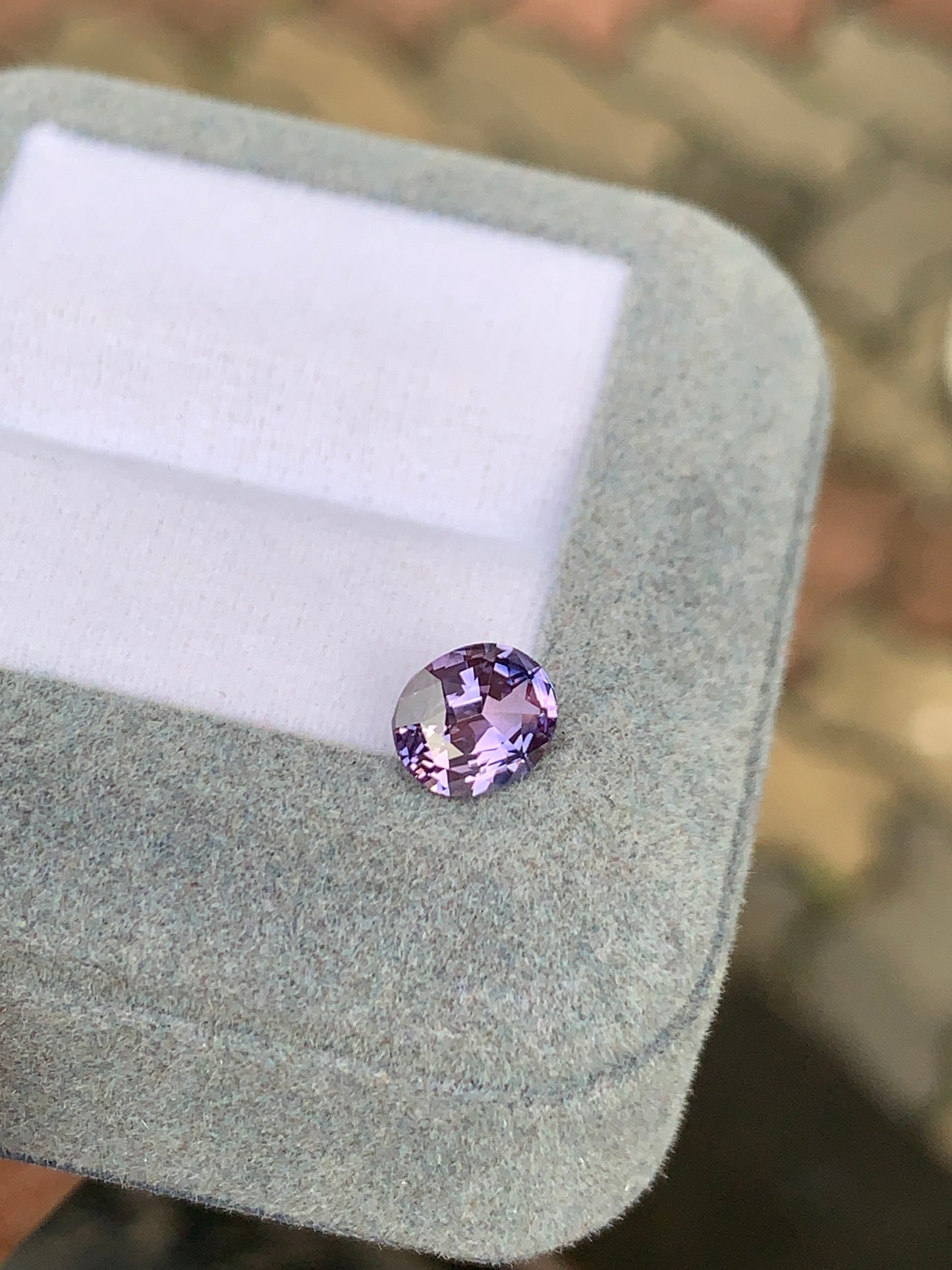 Une pierre précieuse Saphir Violet ronde et étincelante de 1,39 ct de Bonnot Paris repose élégamment sur une boîte recouverte de tissu gris clair sur un fond aux tons terreux.