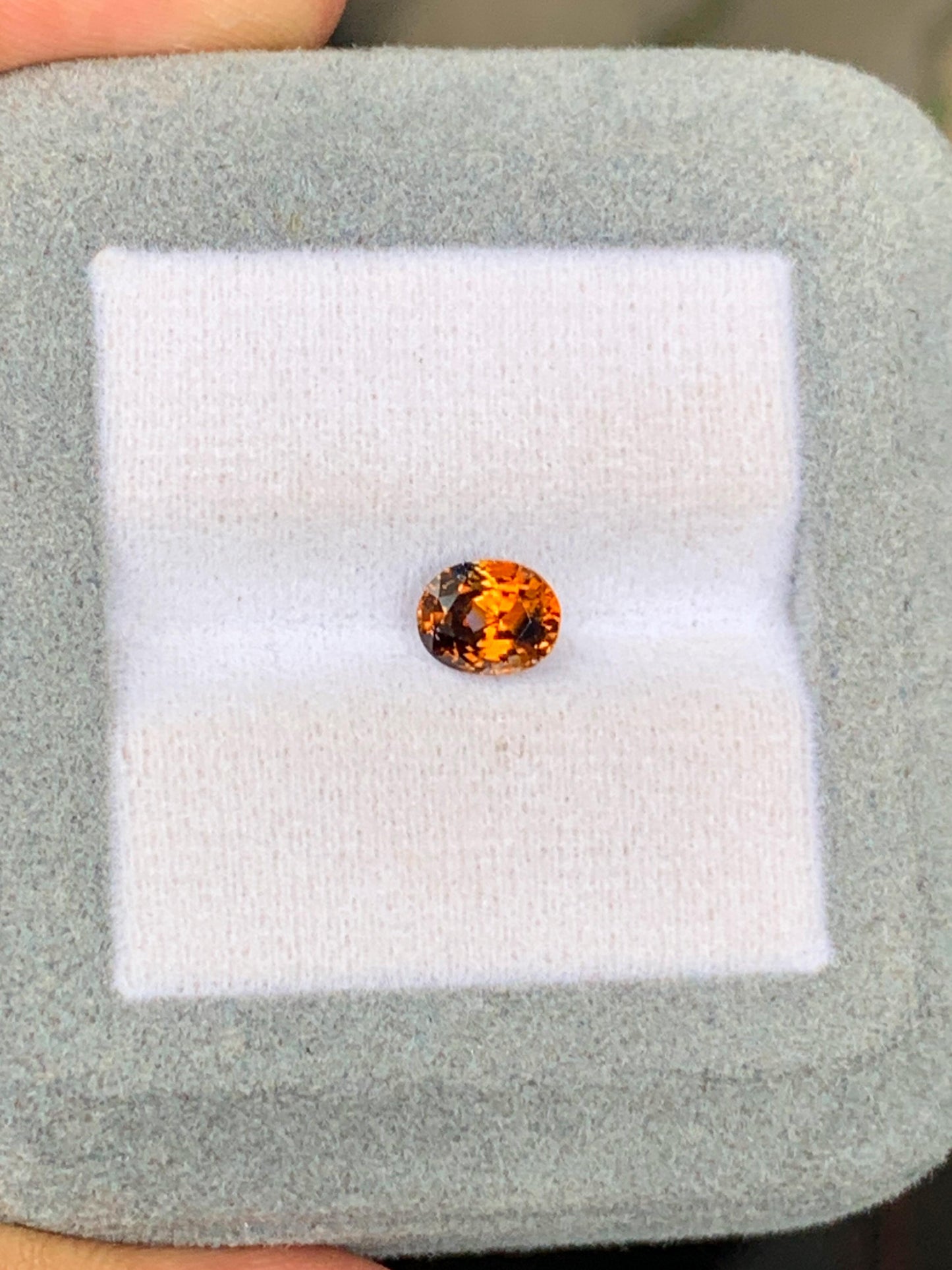 Le Saphir bicolore • 1,13 ct de Bonnot Paris, une pierre précieuse ronde et étincelante d'un orange vif rappelant une pierre précieuse du Sri Lanka, est présenté sur un coussin blanc moelleux dans un cadre gris. Sa teinte vibrante reflète magnifiquement la lumière sur le coussin lisse.