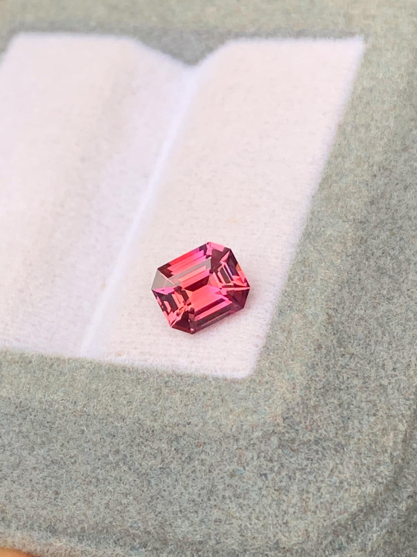 Le Saphir bicolore de 1,12 ct de Bonnot Paris, une pierre précieuse taille émeraude rose, est présenté sur une surface en feutre gris clair avec un fond doucement éclairé.