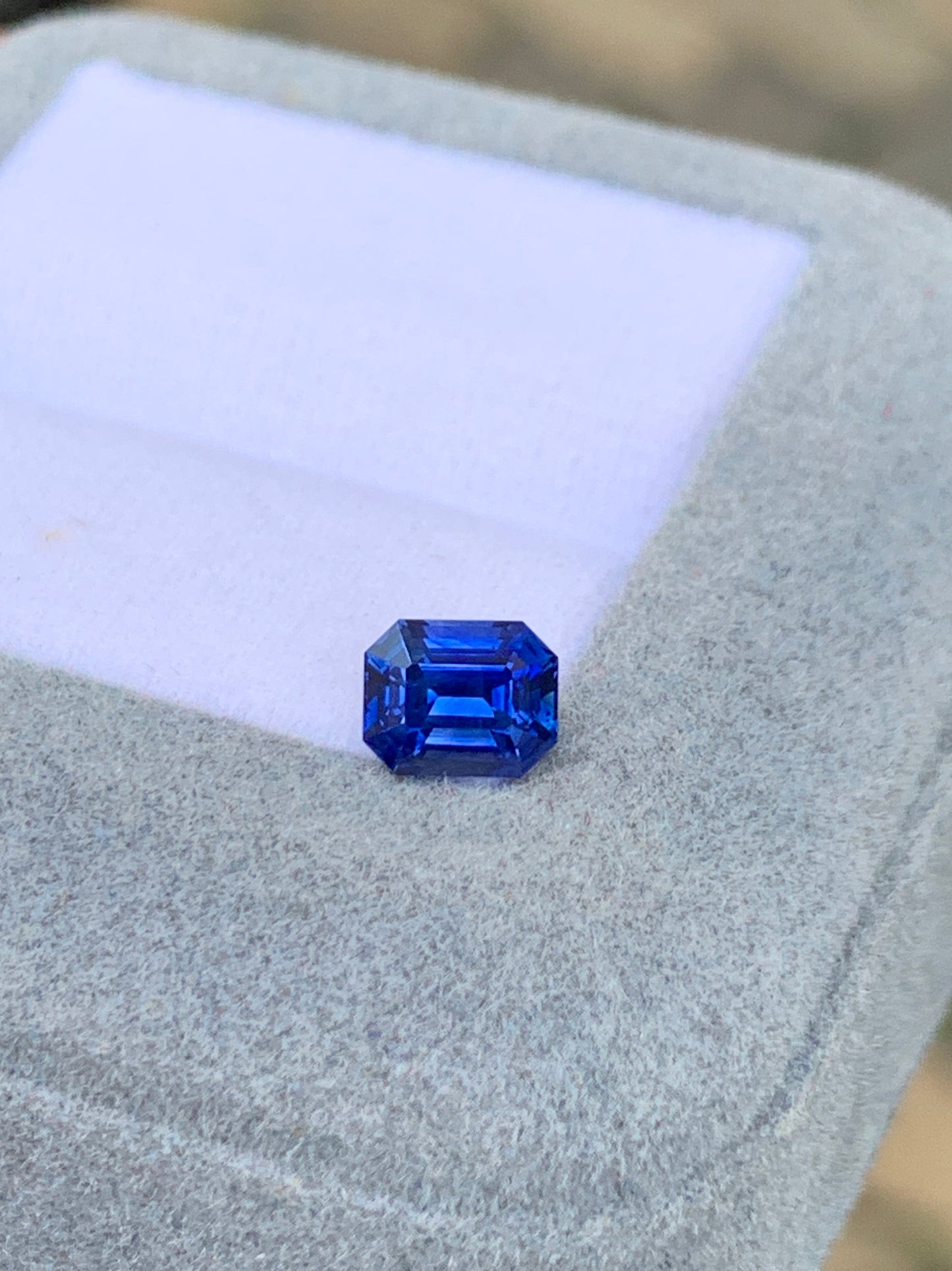 Le Bonnot Paris Saphir bleu • 1,03ct est une pierre précieuse taille émeraude à la teinte vibrante, élégamment présentée dans un coffret à bijoux gris clair avec un intérieur en mousse blanche, mettant en valeur ses facettes uniques.