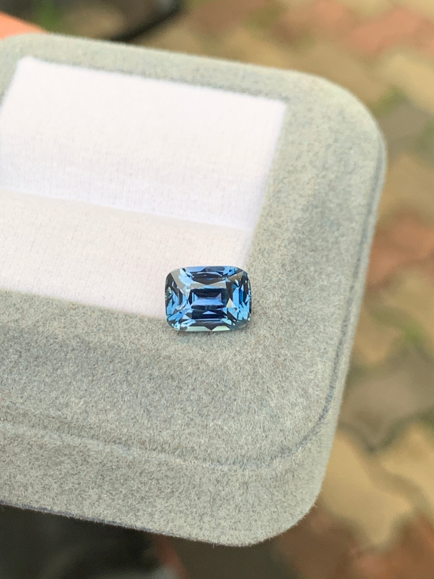 Le Saphir bleu taille rectangulaire de 2,75 carats de Bonnot Paris est présenté dans un écrin de velours gris. Sa rareté, en tant que pierre précieuse, est mise en valeur par un arrière-plan extérieur flou, sublimant ce chef-d'œuvre de joaillerie unique.