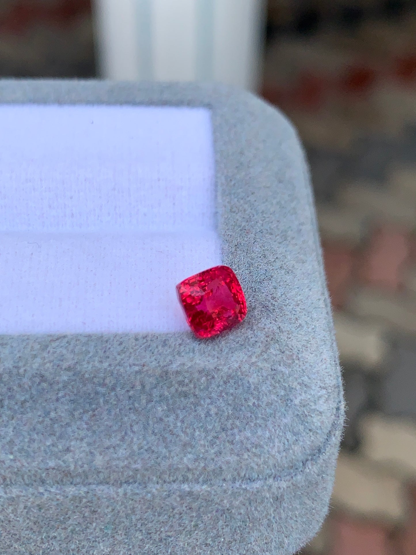 Le Spinelle rouge • 1,54 ct de Bonnot Paris, taille coussin, est élégamment serti sur un tissu gris doux. Ses facettes captent la lumière avec brio, soulignant sa clarté et son éclat, rendant cette pièce rare et captivante.